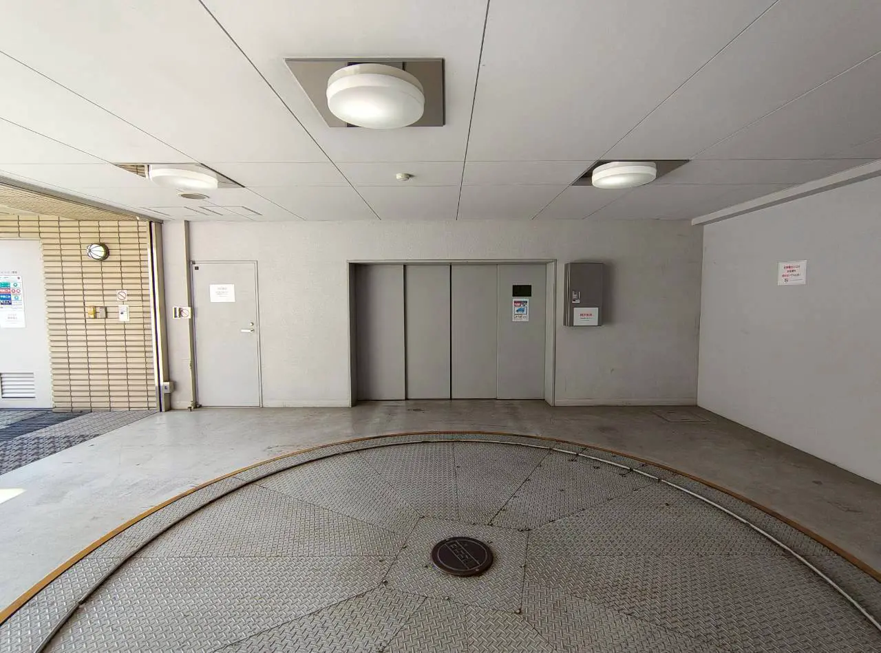 - モダンなエレベーター前のロビー、壁面に掲示物、円形の床と天井照明がある空間