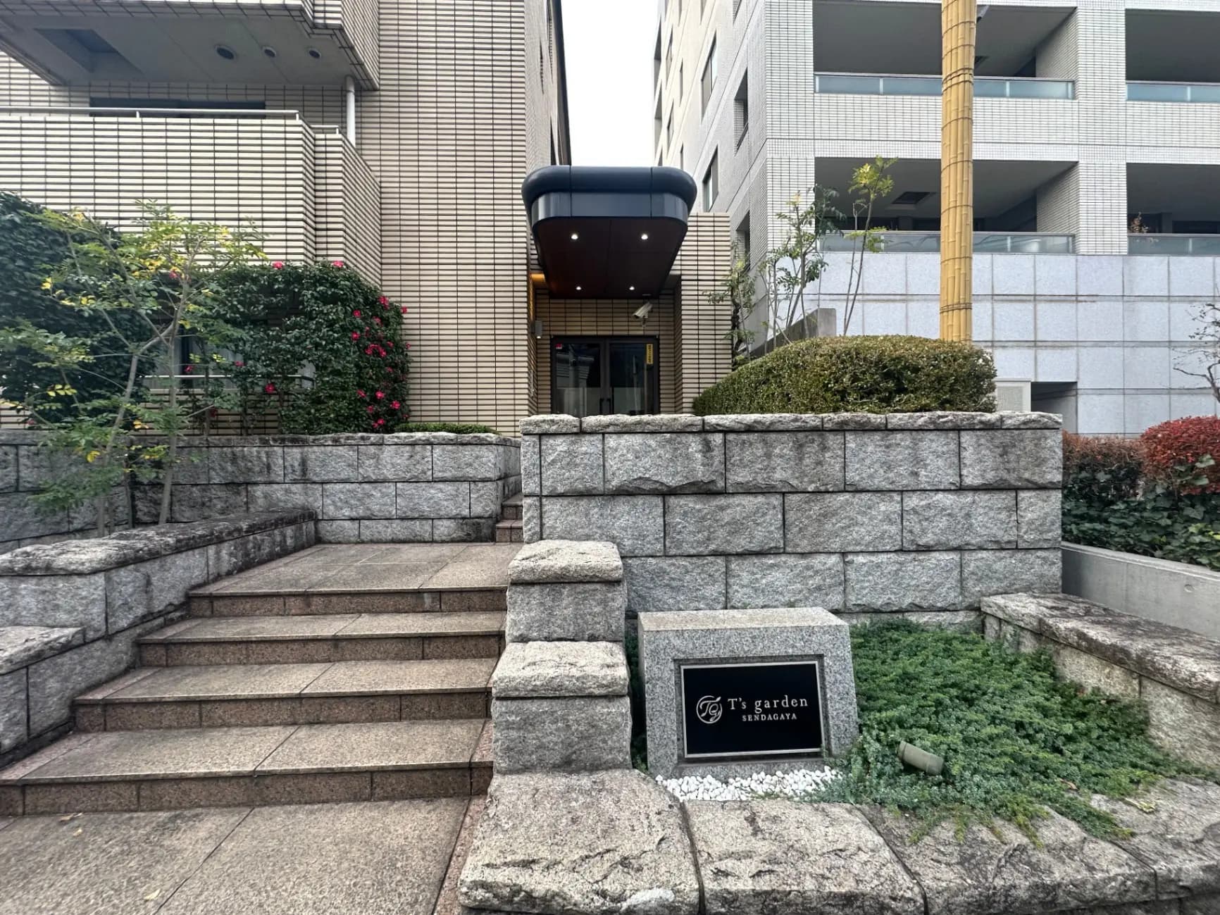 石造りの階段と緑豊かな植栽、T's garden表札があるモダンなオフィスビルのエントランス