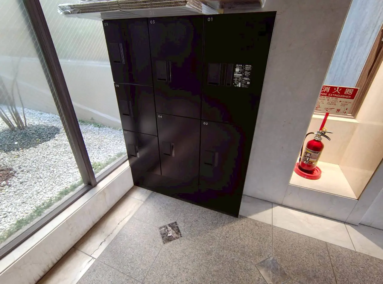 - 黒いロッカーが並ぶエントランス、明るい大きな窓と石の床、奥に消火器が配置された安全対策のスペース