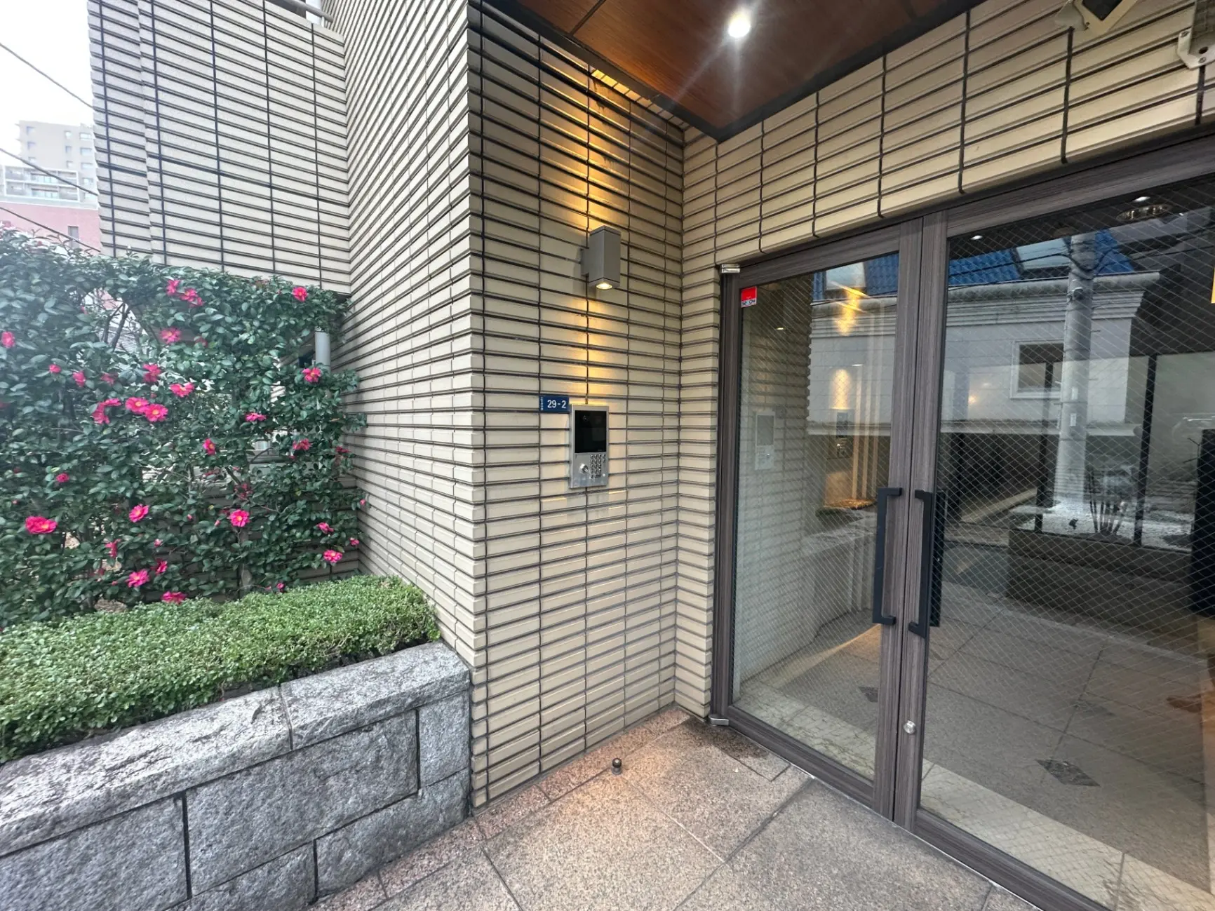 都市のモダンな建物の入口、ストライプ模様の壁、ガラスドア、緑の植栽とピンクの花がある外観