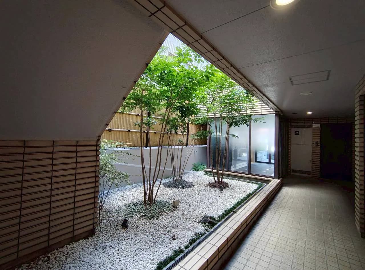 - 自然光が差し込む中庭の景観、植栽に囲まれた白砂利の庭とガラスの壁が特徴的な現代的なエントランスデザイン