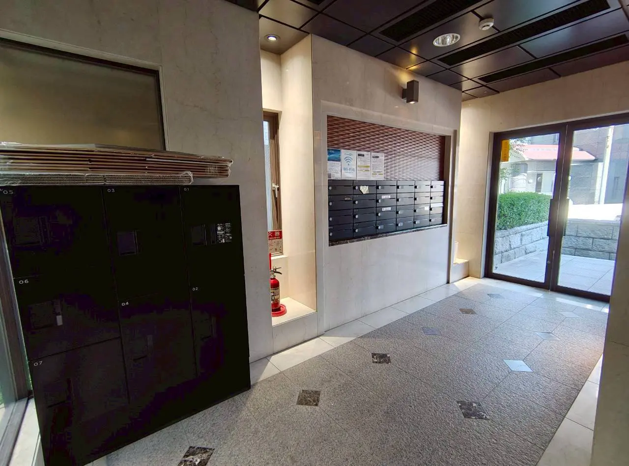 - モダンなエントランスホール、黒いロッカー、郵便受け、ガラスドアの外に明るい庭が見える入口のインテリア