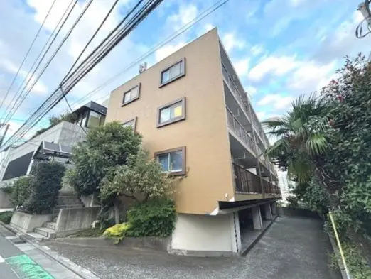 - 駐車場がある三階建てのアパートメント、明るい外壁と周囲の緑が調和する建物の外観