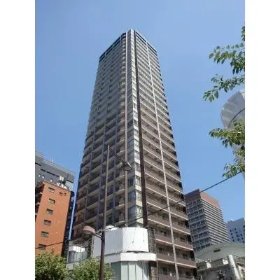 高層マンションの外観、青空を背景にしたモダンなデザインの建物、周囲には都市のビルが立ち並ぶ景観