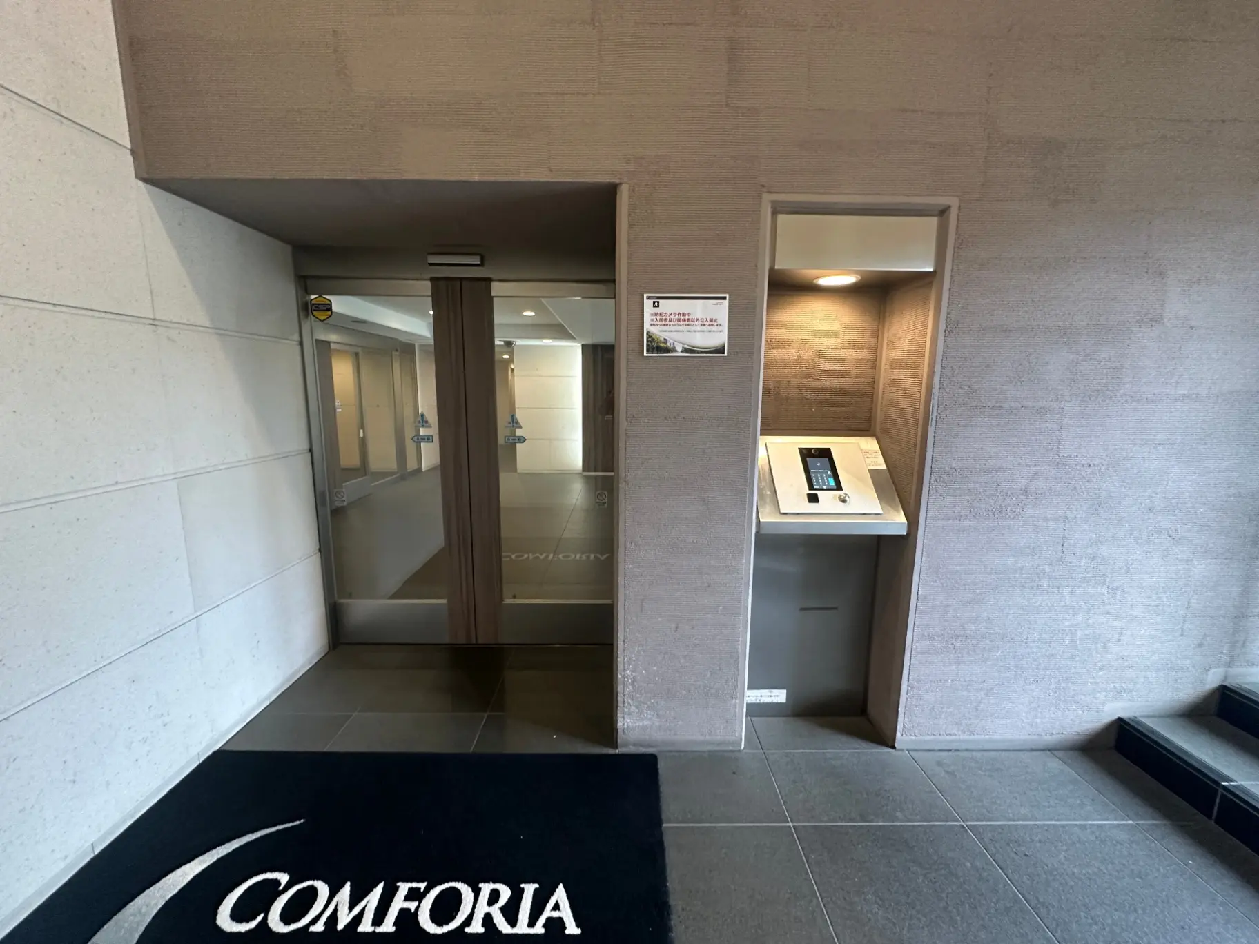 エントランスにあるモダンなオートロックドア、COMFORIAのロゴマット、清潔感のある室内インターフォン設置エリア