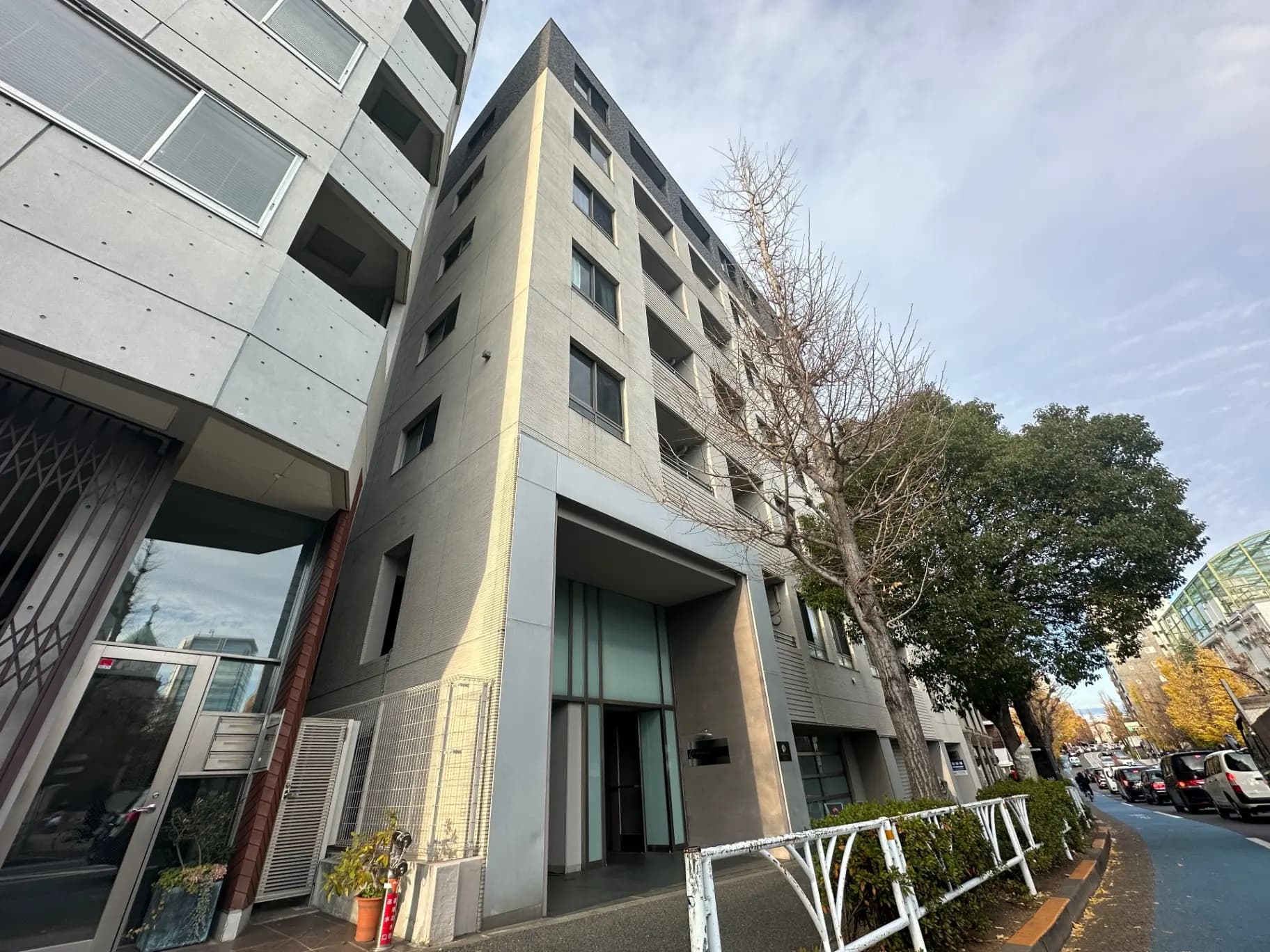 現代的な建築デザインのマンション、都市の住宅街に位置し、通り沿いの木々とクリアな青空