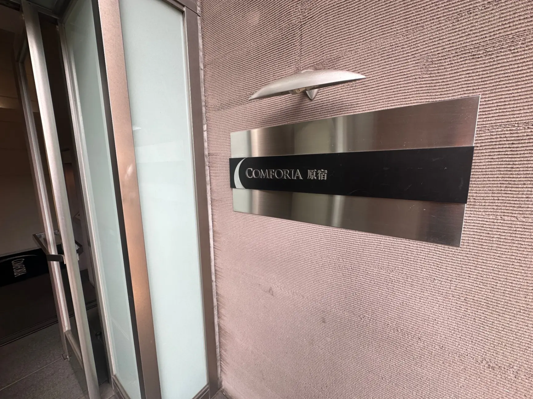 エントランスの壁に取り付けられたモダンな看板、COMFORIAブランドのロゴと質感のある壁面