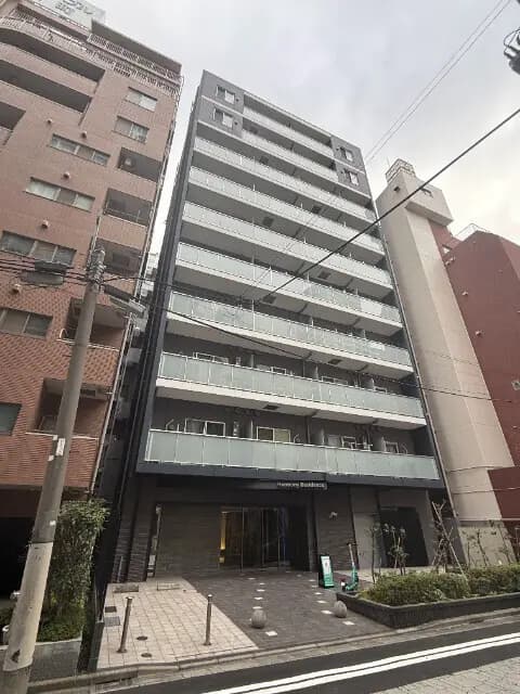 - 近代的なデザインの高層マンション、バルコニー付きの外観、周囲には他のビルと商業施設が立ち並ぶ都市風景