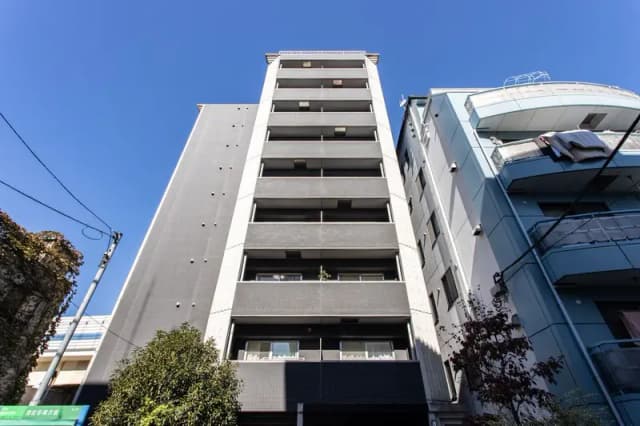 - 都市部にあるモダンなマンションの外観、グレーの壁とバルコニーを持つ5階建ての建物、青空を背景にした景観