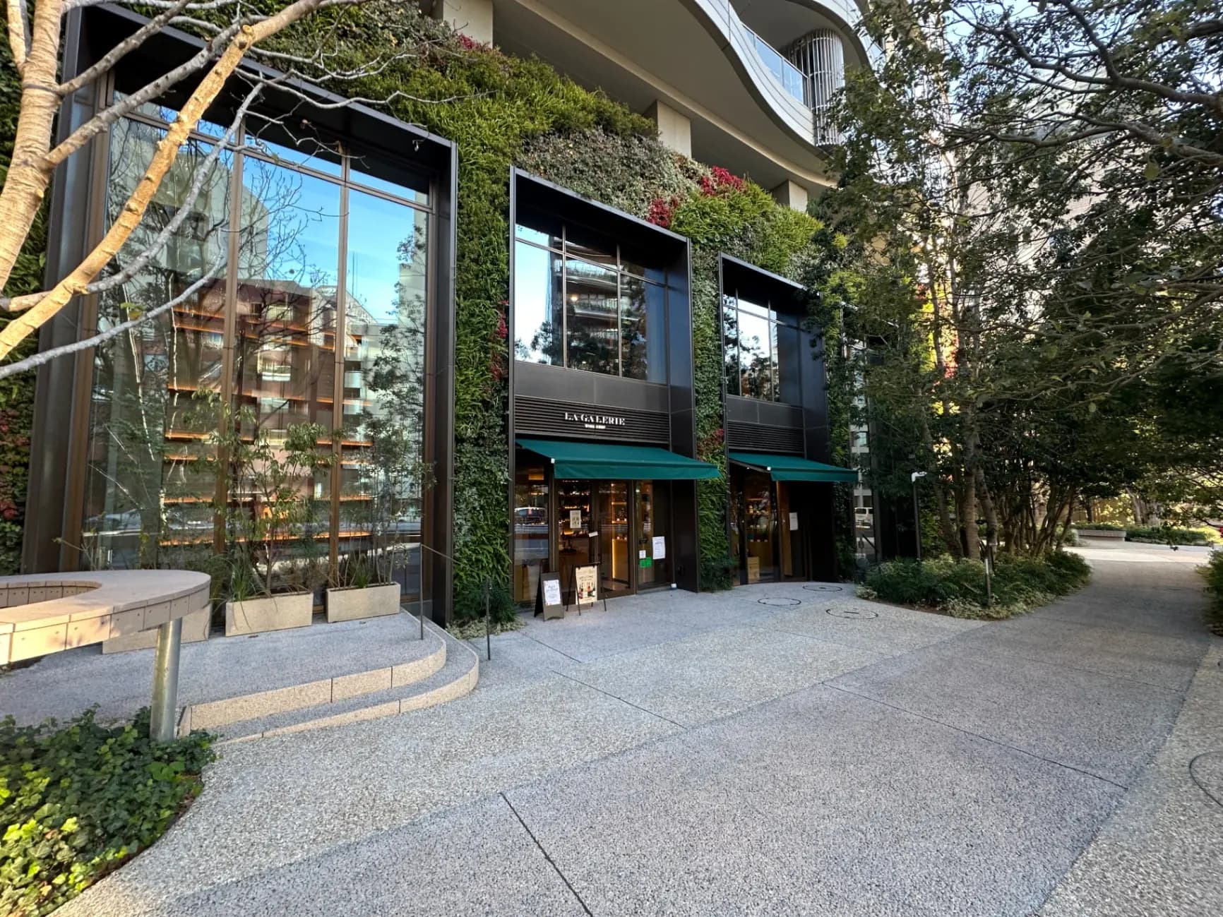 モダンな建築スタイルの店舗入り口、ガラス窓と緑の植物が印象的な外観デザイン
