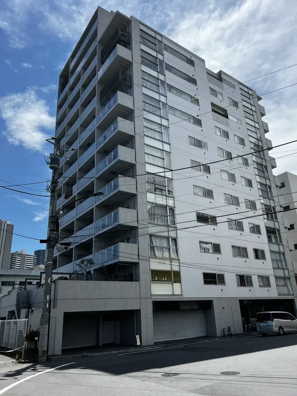 - 近代的なデザインのマンション外観、バルコニー付きの階層構造、青空と電線が交錯する都市の風景