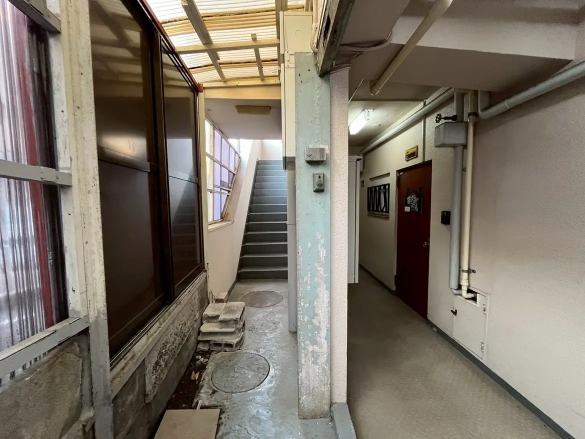 - 明るい階段と廊下、建物内の通路に階段が続き、壁には配管が見えるシンプルなデザインのインテリア