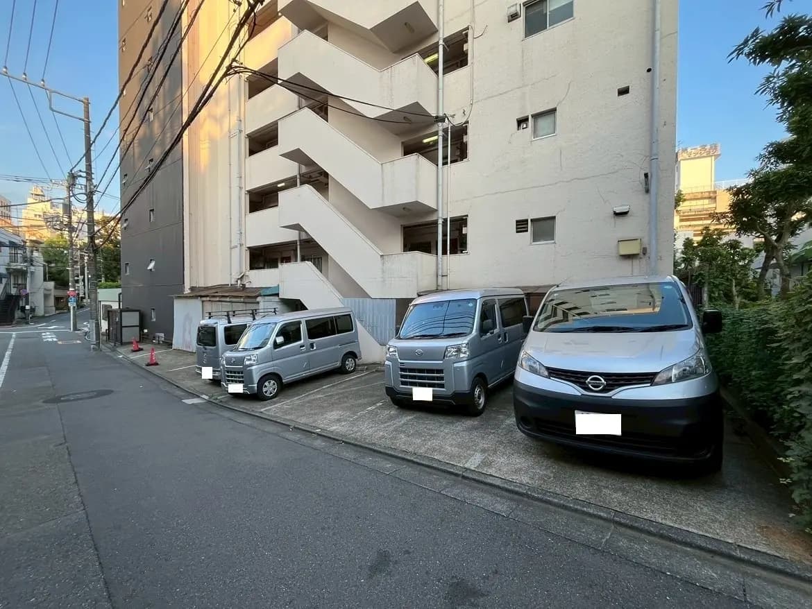 - 駐車場に停まっている複数の車、周囲にはマンションの外観が映る都市の風景