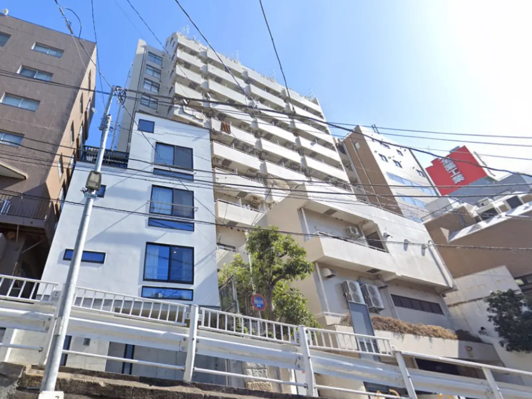 - 高層マンションと低層の白い建物が並ぶ街並み、青空と電線が広がる風景