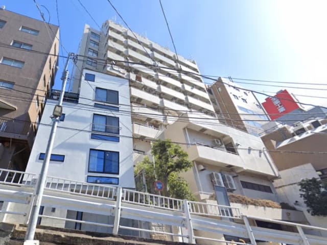 - 高層マンションと低層の白い建物が並ぶ街並み、青空と電線が広がる風景