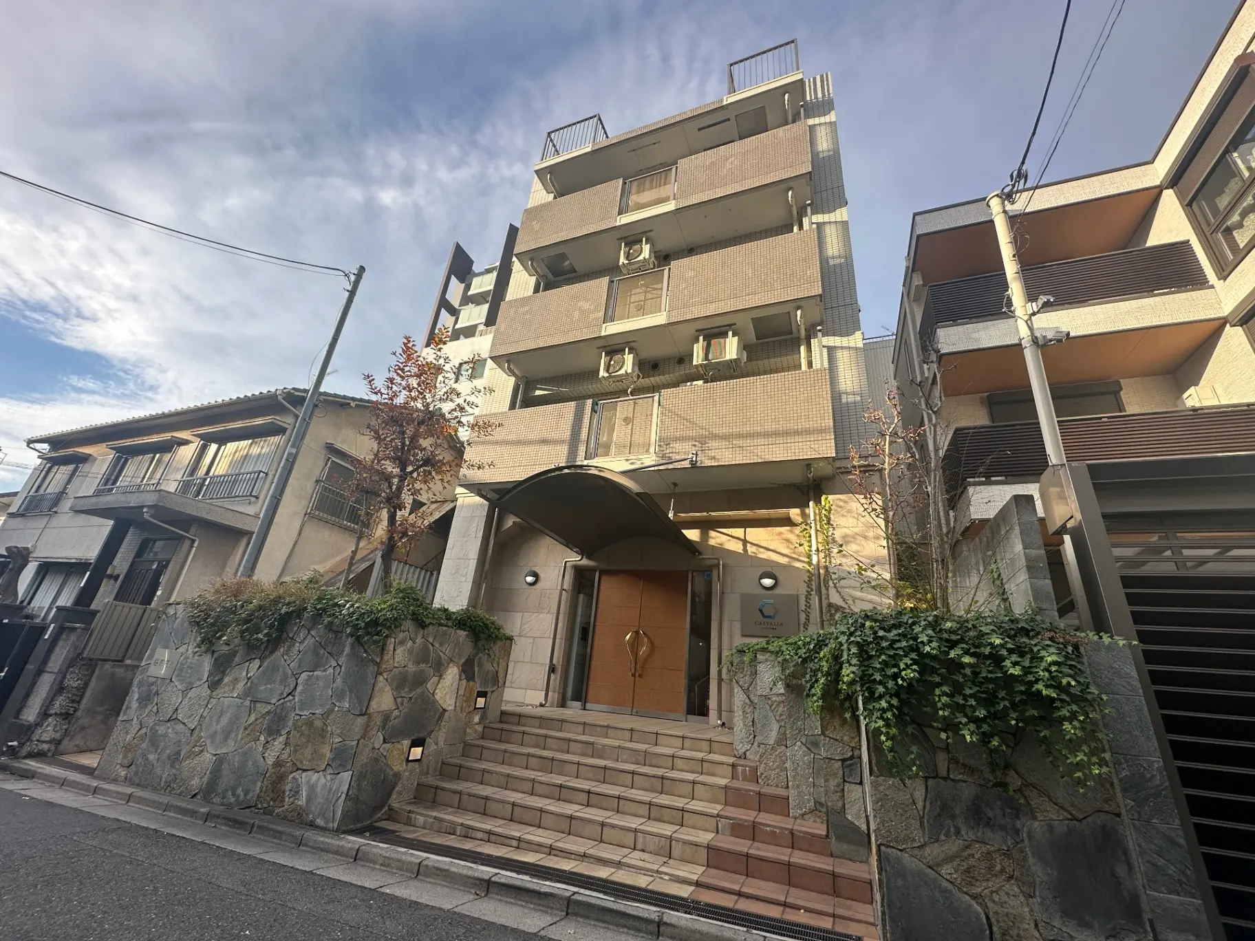 都市部に位置する現代的なマンションの外観、天然石の壁と階段が特徴的なエントランス