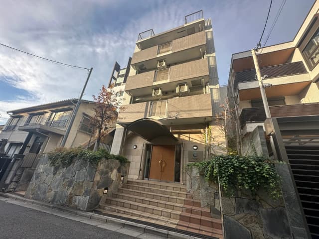 都市部に位置する現代的なマンションの外観、天然石の壁と階段が特徴的なエントランス