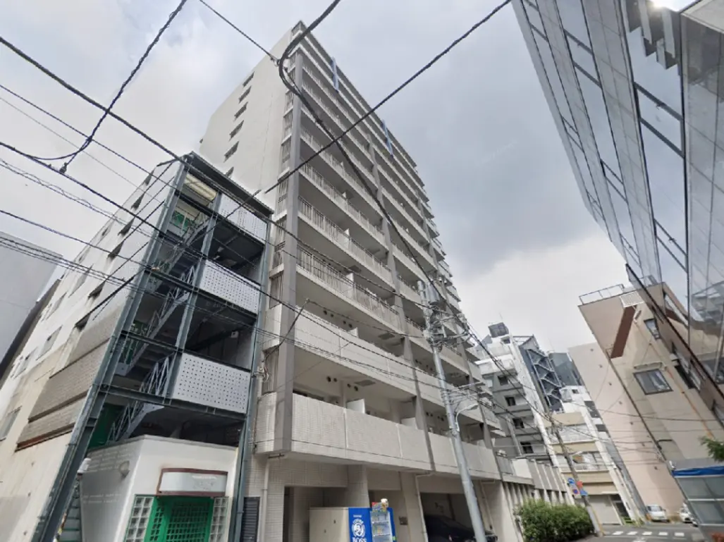 - 都市型マンションの外観、右側に近代的なガラス張りのビル、電線が交錯する街並みの様子