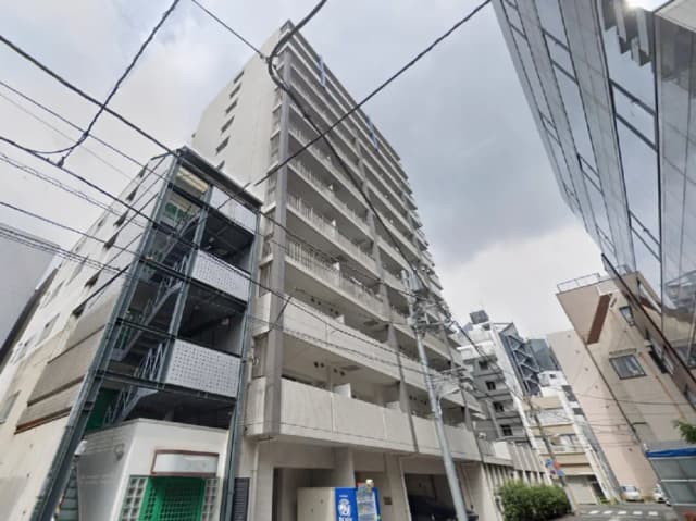 - 都市型マンションの外観、右側に近代的なガラス張りのビル、電線が交錯する街並みの様子