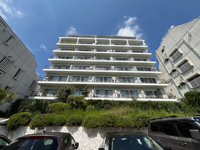 - 大きな窓とバルコニーが付いた白い外観の高層マンション、周囲には手入れされた緑の景観が広がる