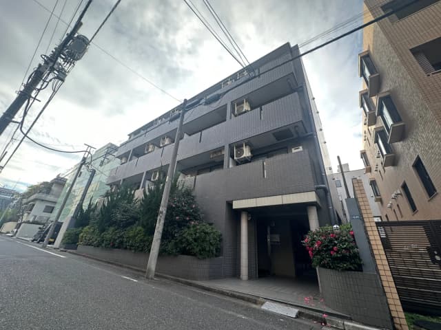 現代的な外観のマンションビル、植栽が施されたエントランス、市街地に位置する住宅街