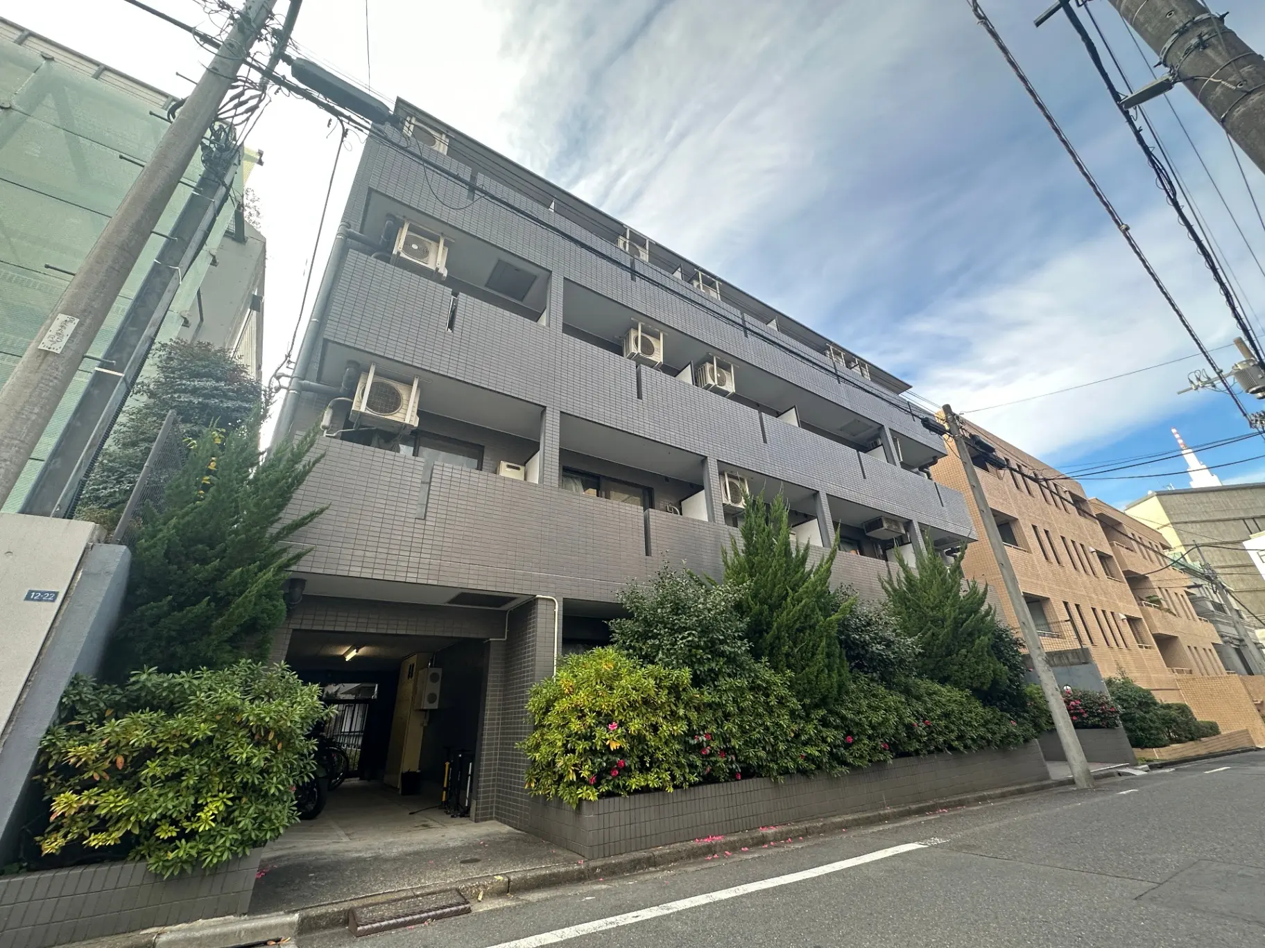 都市部に位置する現代的なアパートの外観、緑豊かな植栽とクリアな青空