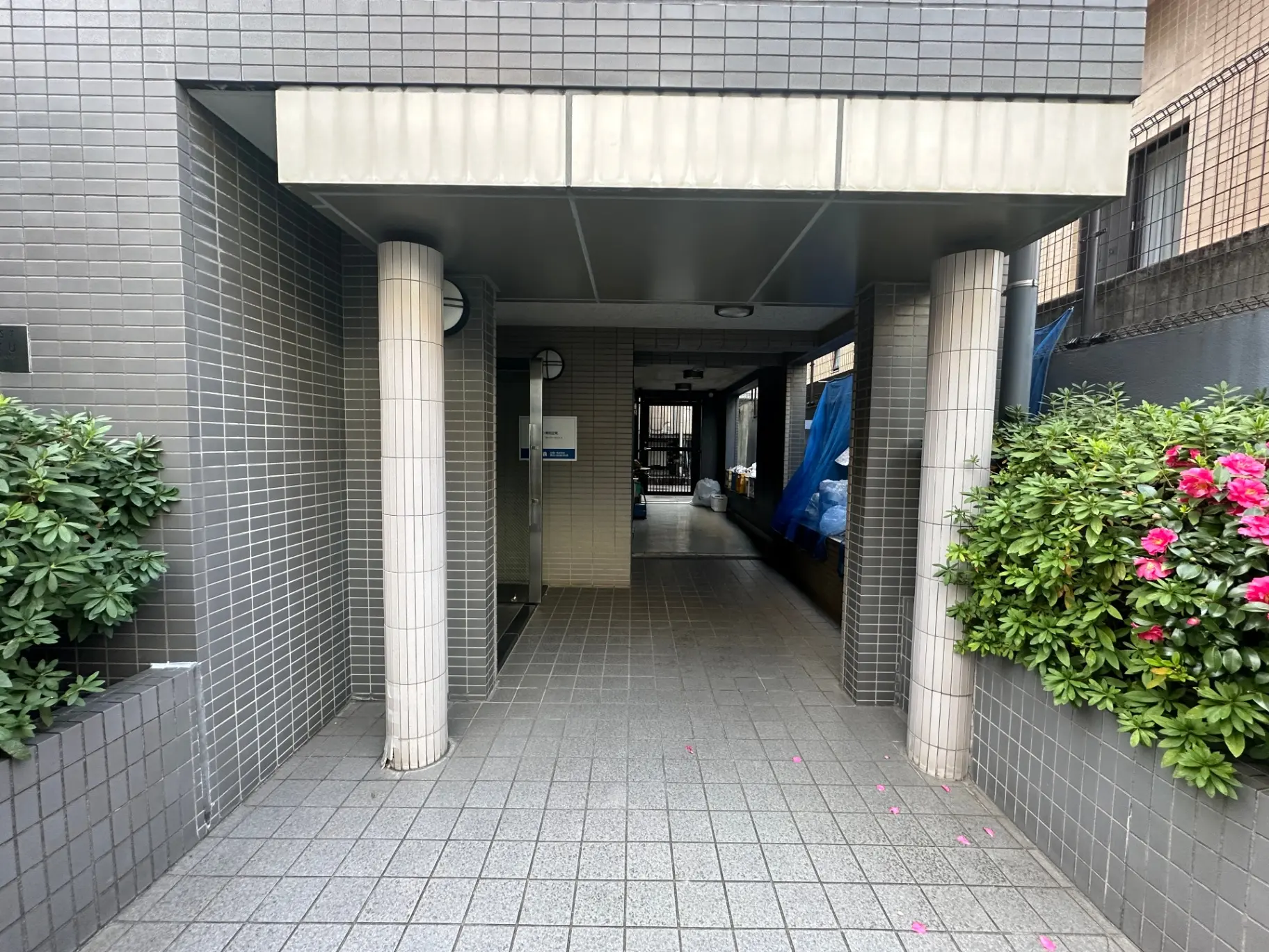 モダンな建物の入り口と通路、タイルで装飾された壁面、緑植物と花がある都市のアパートメント