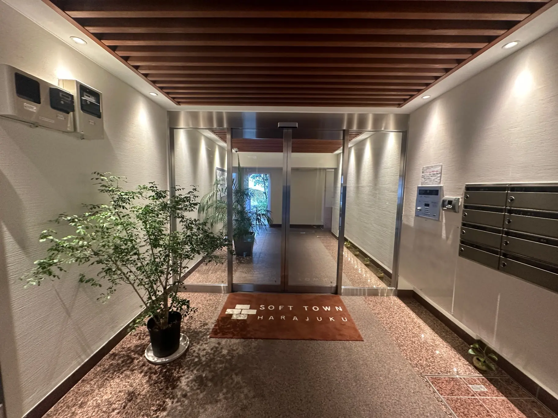 モダンなマンションのエントランスホール、植物の装飾が施された温かみのある照明と木目調の天井デザイン