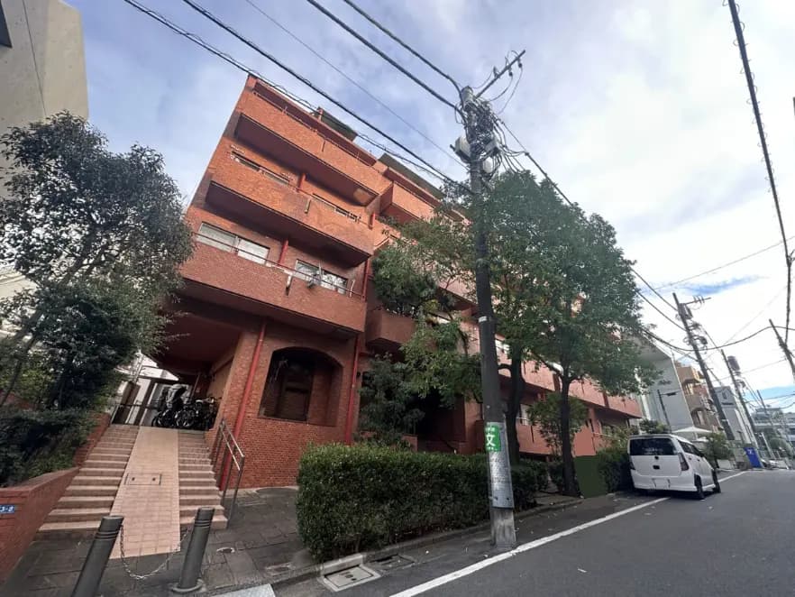 都市部に位置する赤レンガの外観を持つマンション、階段入り口と緑豊かな植栽