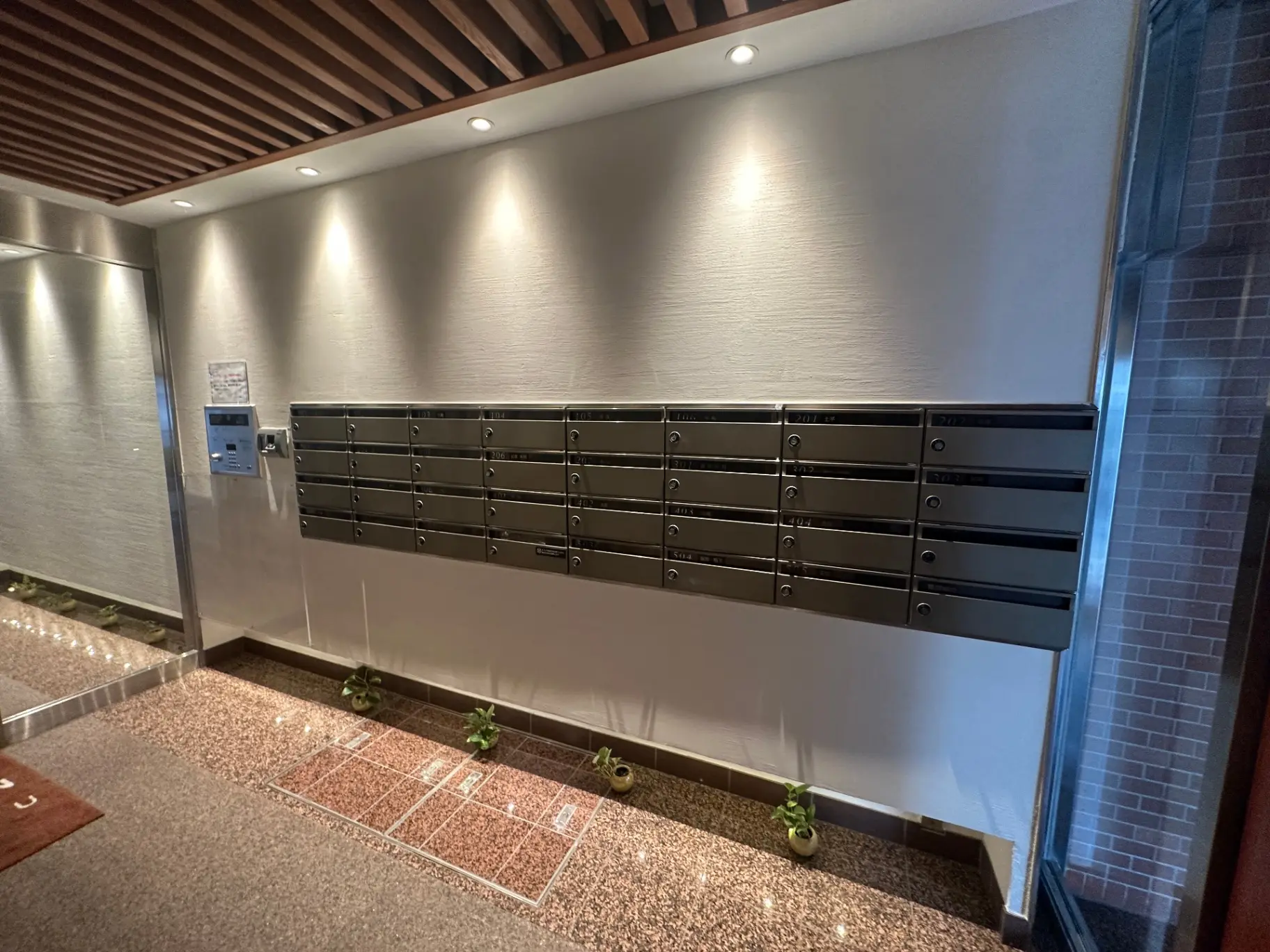 マンションのエントランスにあるシックなメールボックス、清潔でモダンなデザイン、照明付き