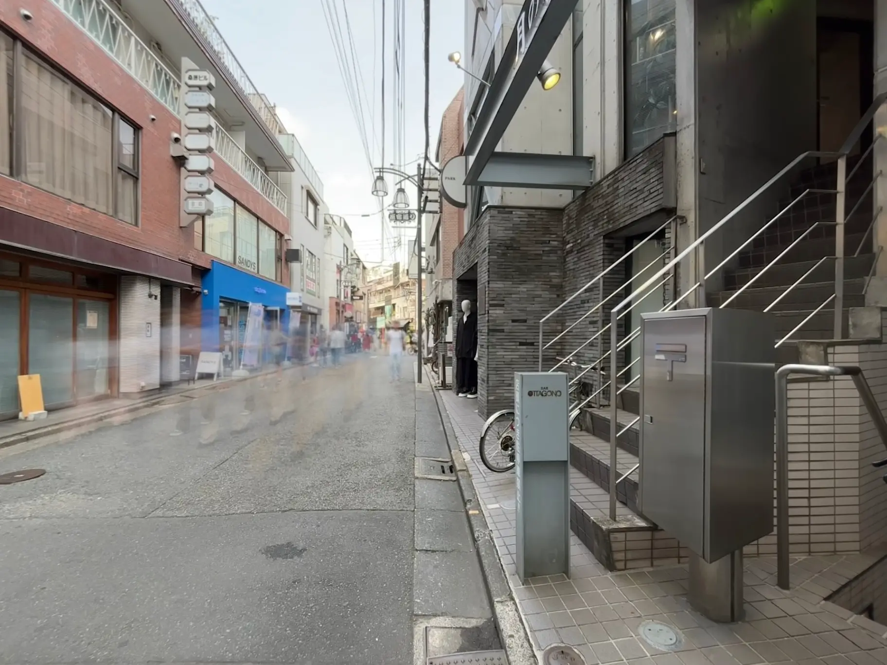 - 賑やかな商店街の通り沿いにあるビル、歩行者や自転車が行き交い、スタイリッシュな看板が並ぶ風景