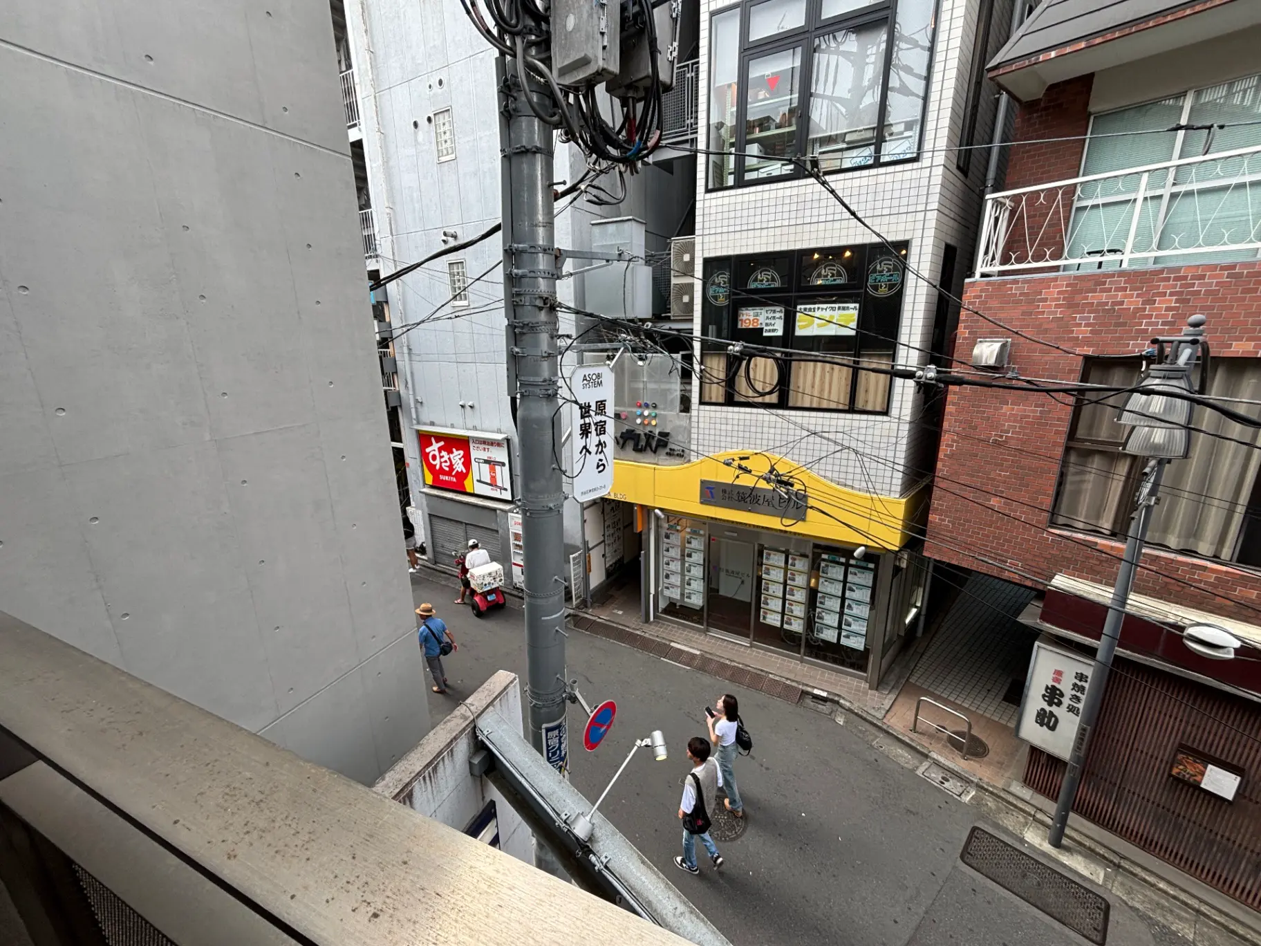 - 都市の街角、電線や看板、通行人が行き交う様子、コンクリートとレンガの建物が立ち並ぶ景観