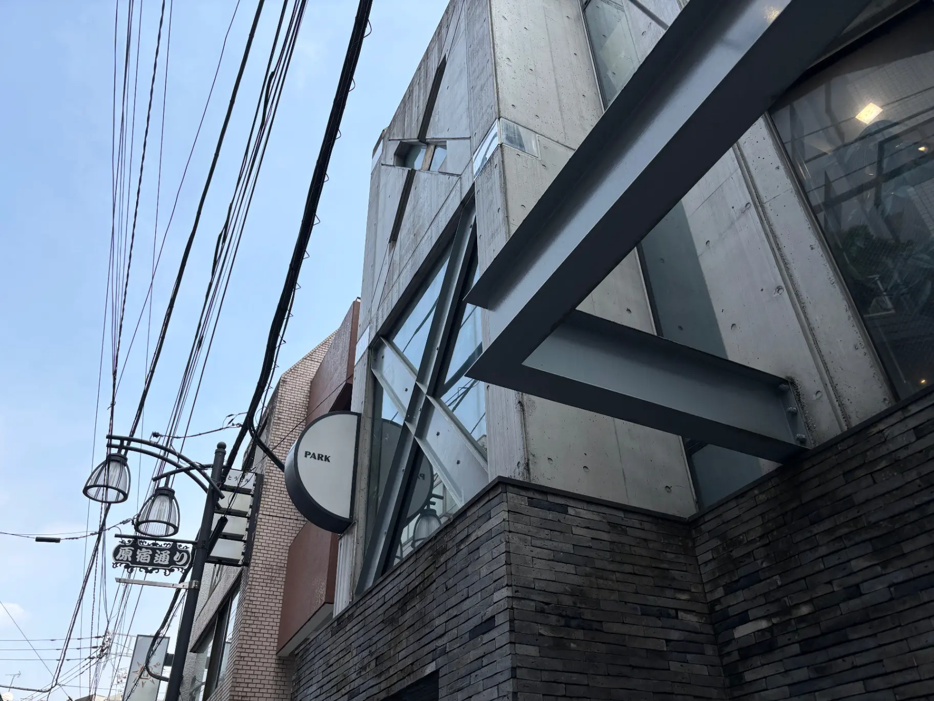 - 現代的なデザインの建物外観、コンクリートとガラスの組み合わせ、看板「PARK」と周囲の電線が見える都市の風景