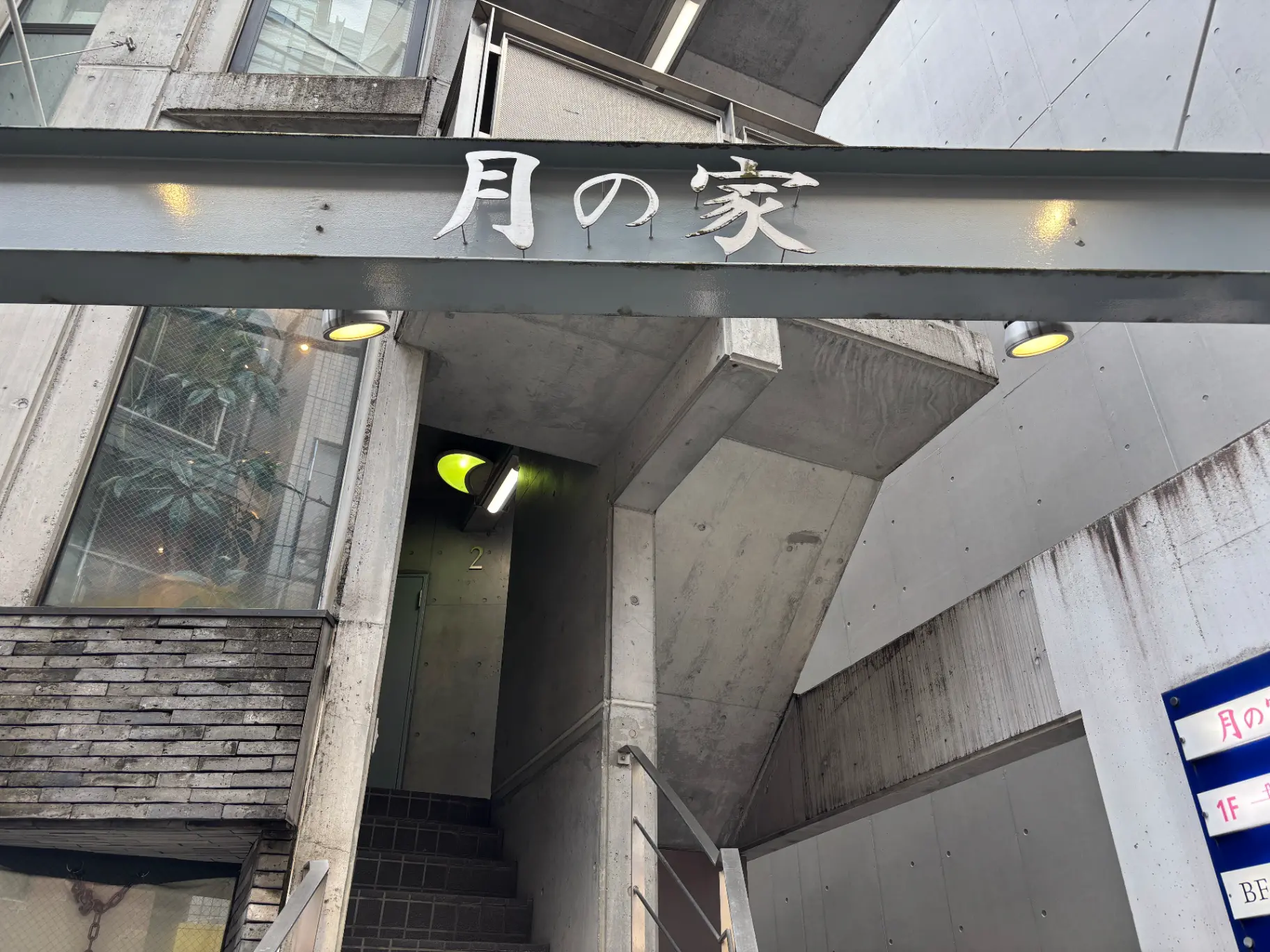 - コンクリート製の外観を持つ「月の家」の入り口、照明が付いた階段と透明な窓越しに見える観葉植物のディテール。