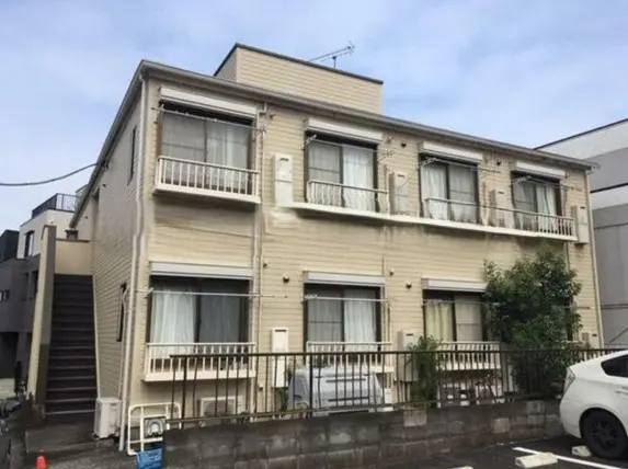- 外観が淡いクリーム色のアパートメント、バルコニー付きの窓が並ぶ二階建て、駐車場と植栽のある風景