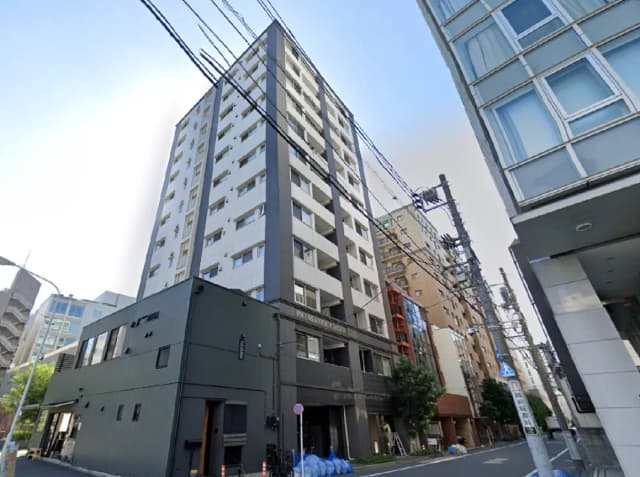 - 都市的な環境に立つモダンなマンション、手前には黒い外壁の建物と電線が見える風景