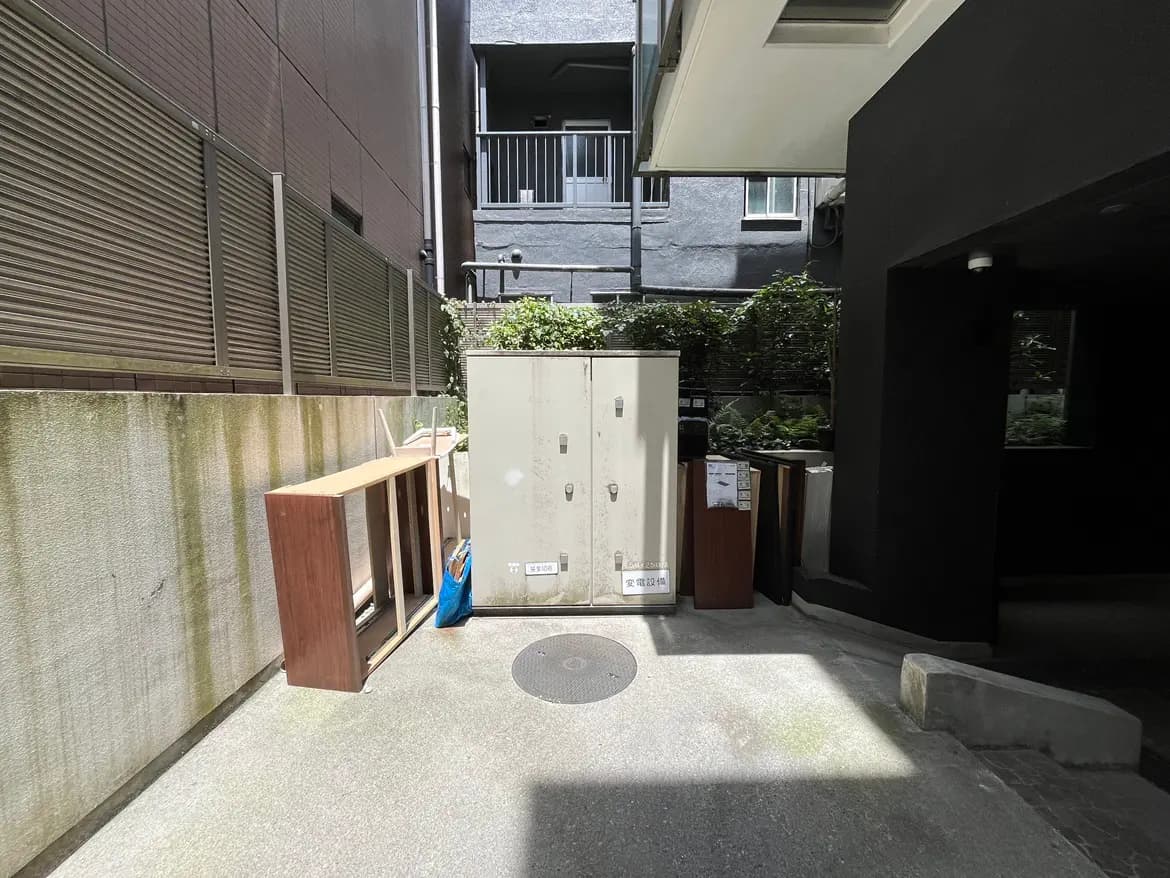 狭い通路に置かれた大きなロッカーと廃棄された家具、周囲に緑が見える住宅エリアのビジュアル