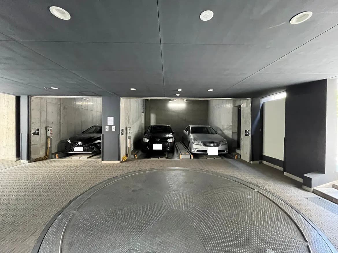- モダンな地下駐車場、車両用リフトの近くに並ぶ3台の車、滑らかなコンクリートの壁と天井のデザイン