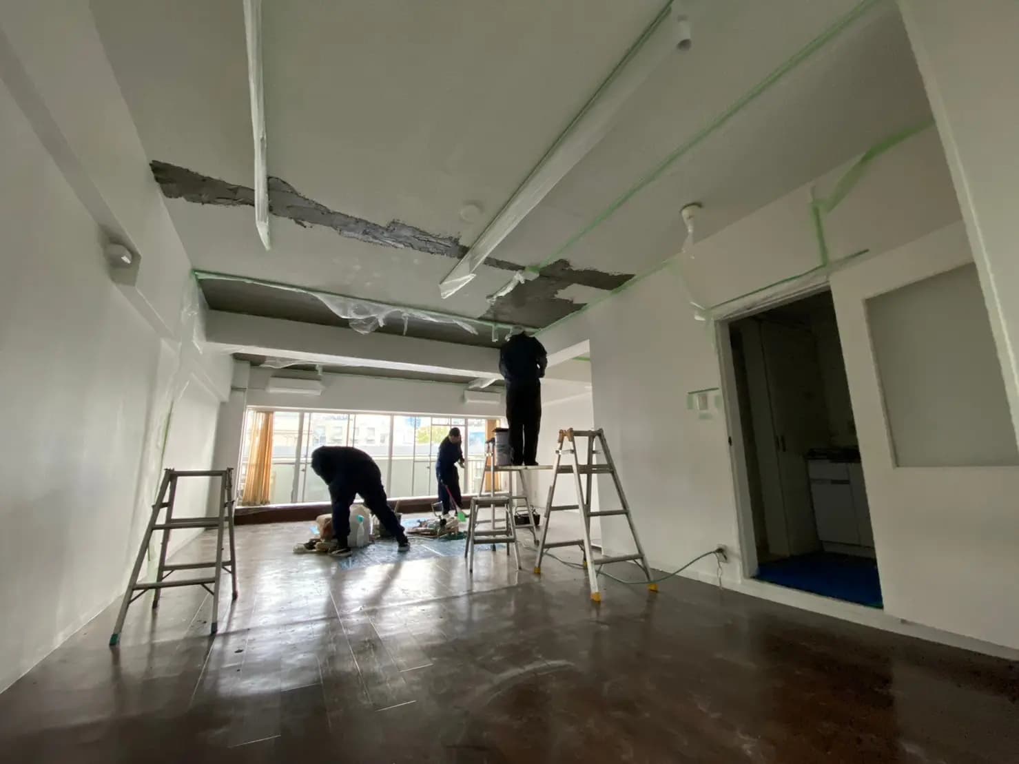 改装中の部屋、作業員がペンキ塗りをしている様子、はしごと工具が置かれたインテリア工事現場