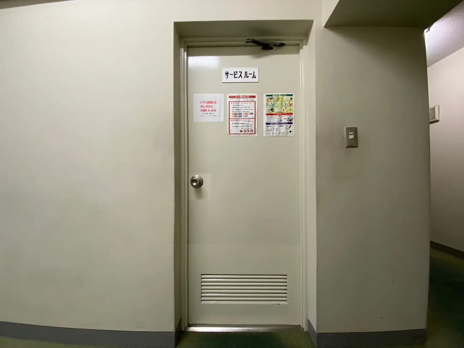 建物の非常口ドア、壁には安全情報の掲示物とサーモスタットがある廊下