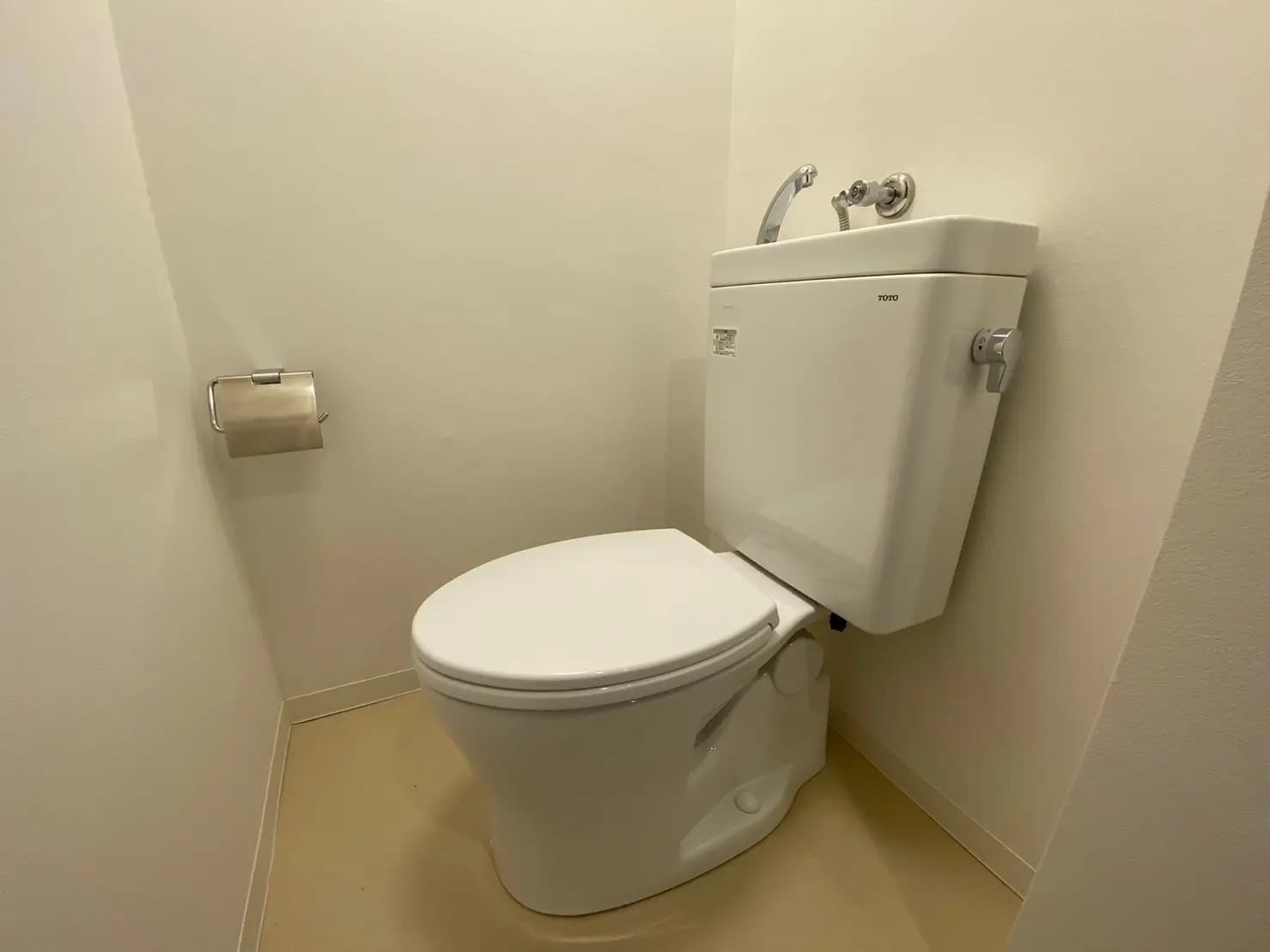 シンプルなデザインのトイレ、壁掛けトイレットペーパーホルダーとタンク式便器が見えるインテリア