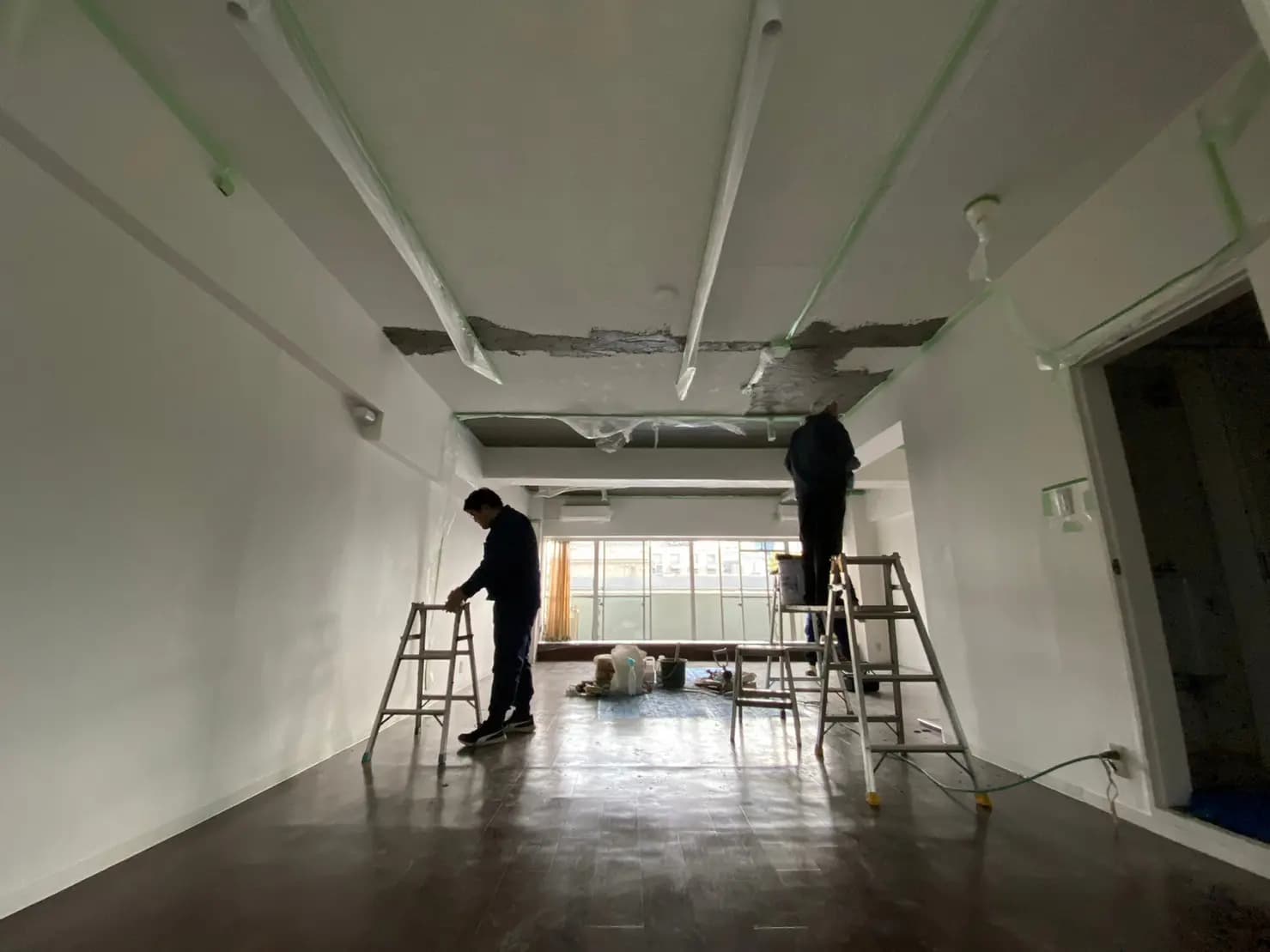 改装中のオフィス空間、梯子に乗る作業員、床の養生作業と開放的な窓
