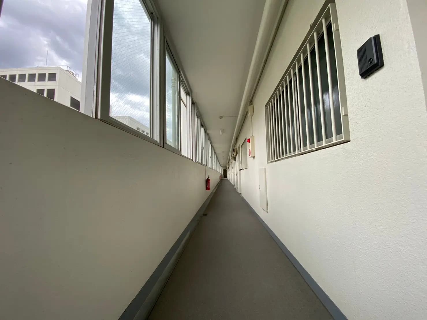 長い廊下と両側の窓、壁に取り付けられた消火器とインターフォン、オフィスビルの内部デザイン