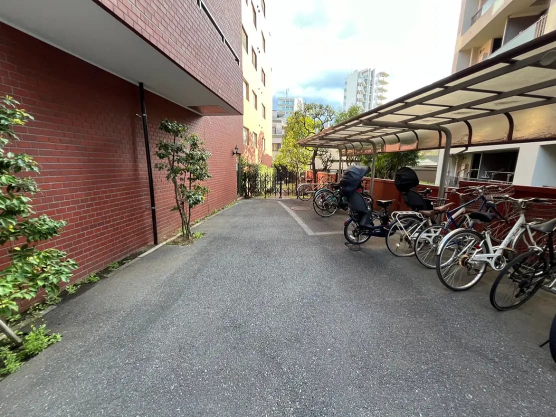 - ブロック壁に囲まれた自転車置き場、整然と並ぶ自転車と周囲の緑が美しい風景