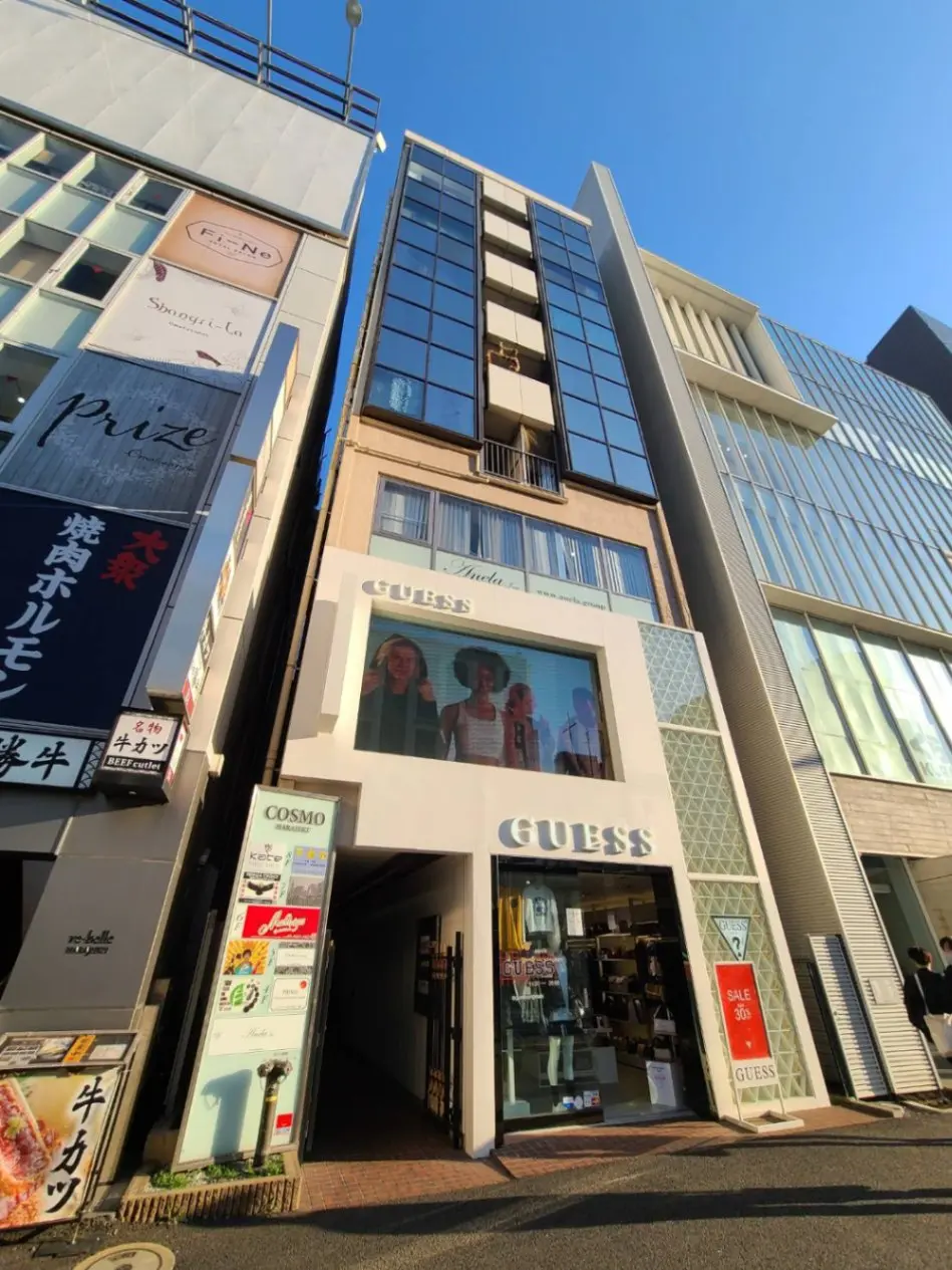 都市地区にあるファッションブランドの店舗外観、ブルーの空と周囲のビル、隣接するレストランや他のショップの看板