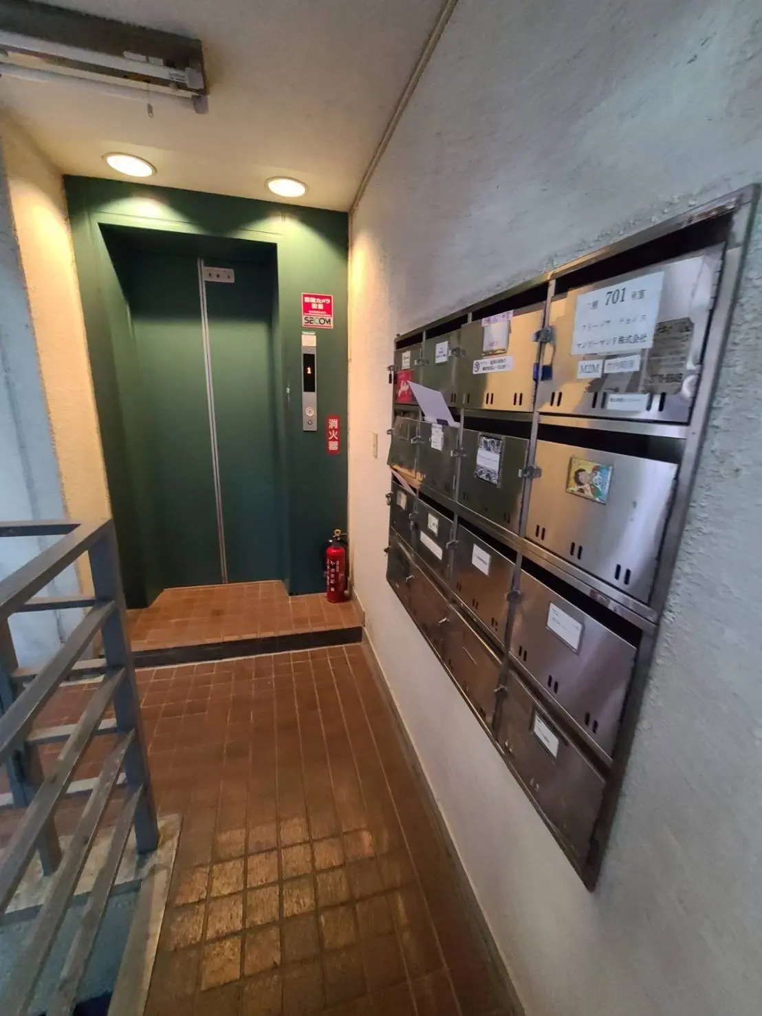 マンションの室内通路と郵便受け、エレベーターの入り口と消火器、照明のある建物内部