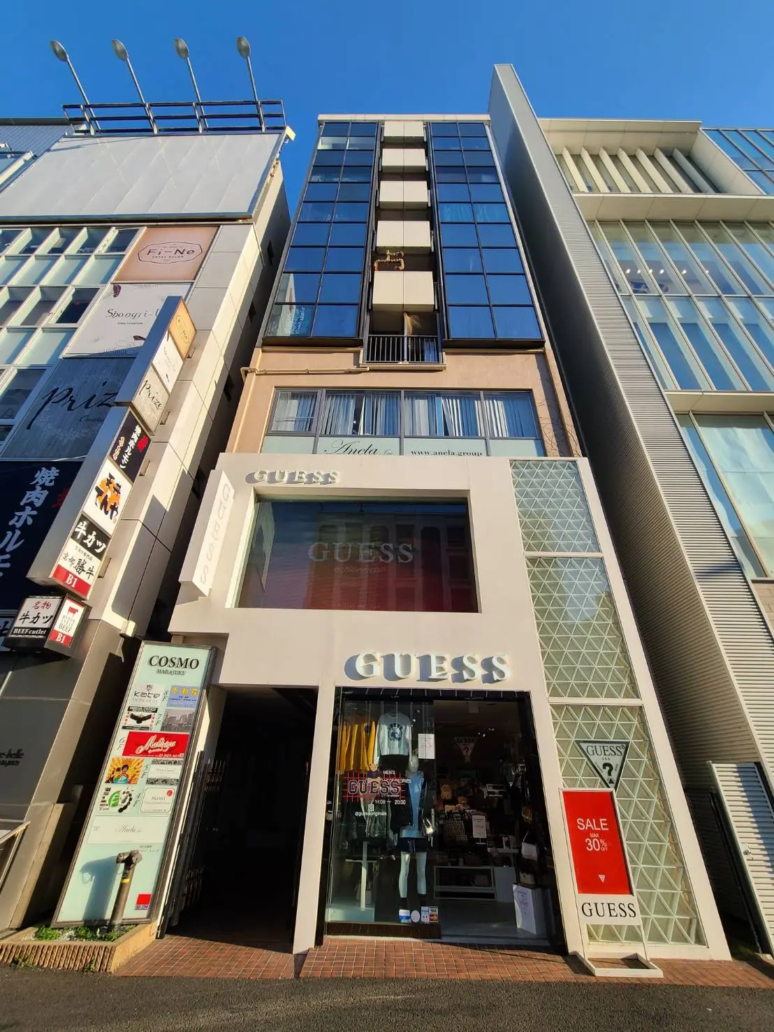 商業ビルのファサード、GUESSブランドの店舗エントランス、クリアな青空と建築デザイン