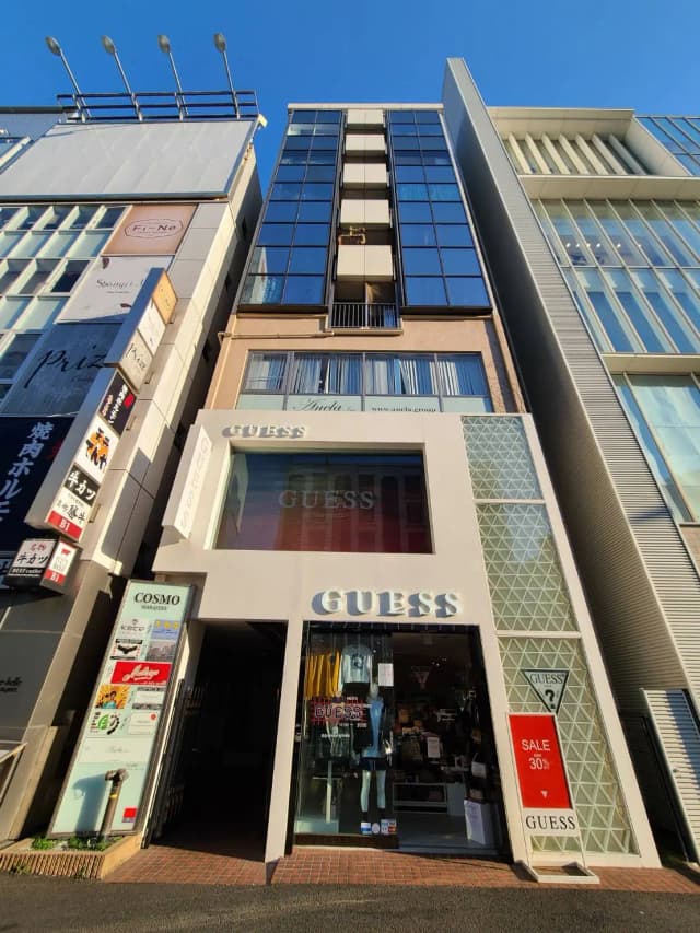 商業ビルのファサード、GUESSブランドの店舗エントランス、クリアな青空と建築デザイン
