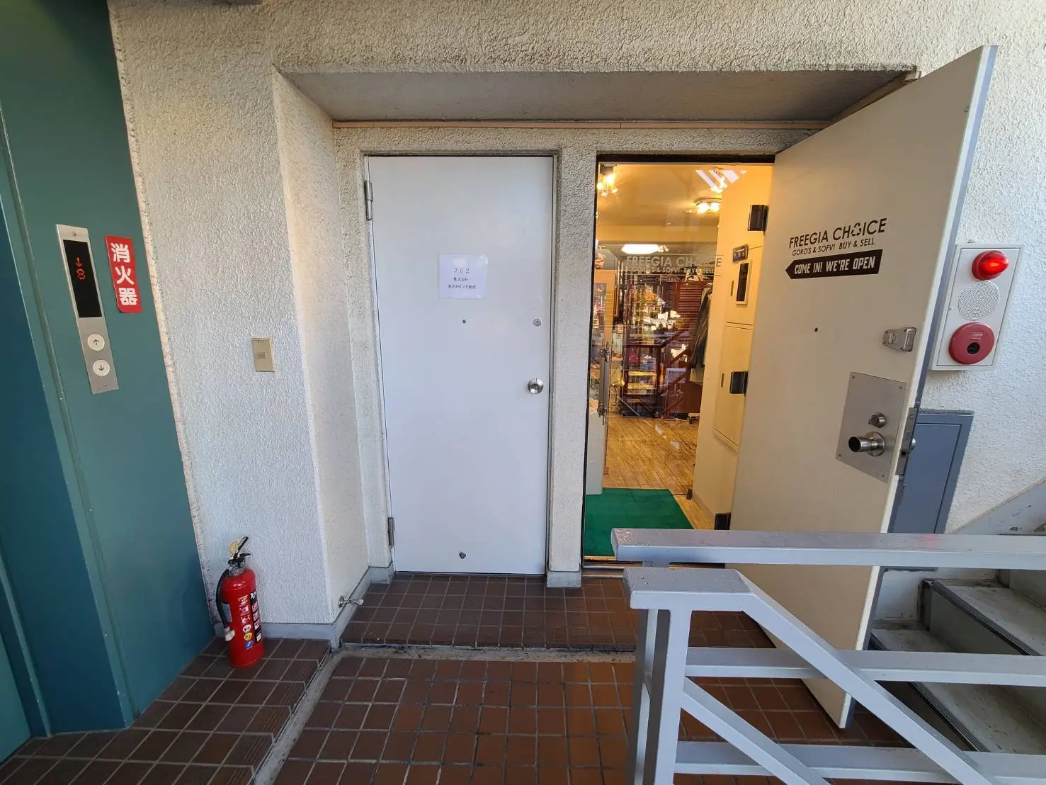 店舗入口とエレベーター、非常階段の標識があるビルの通路