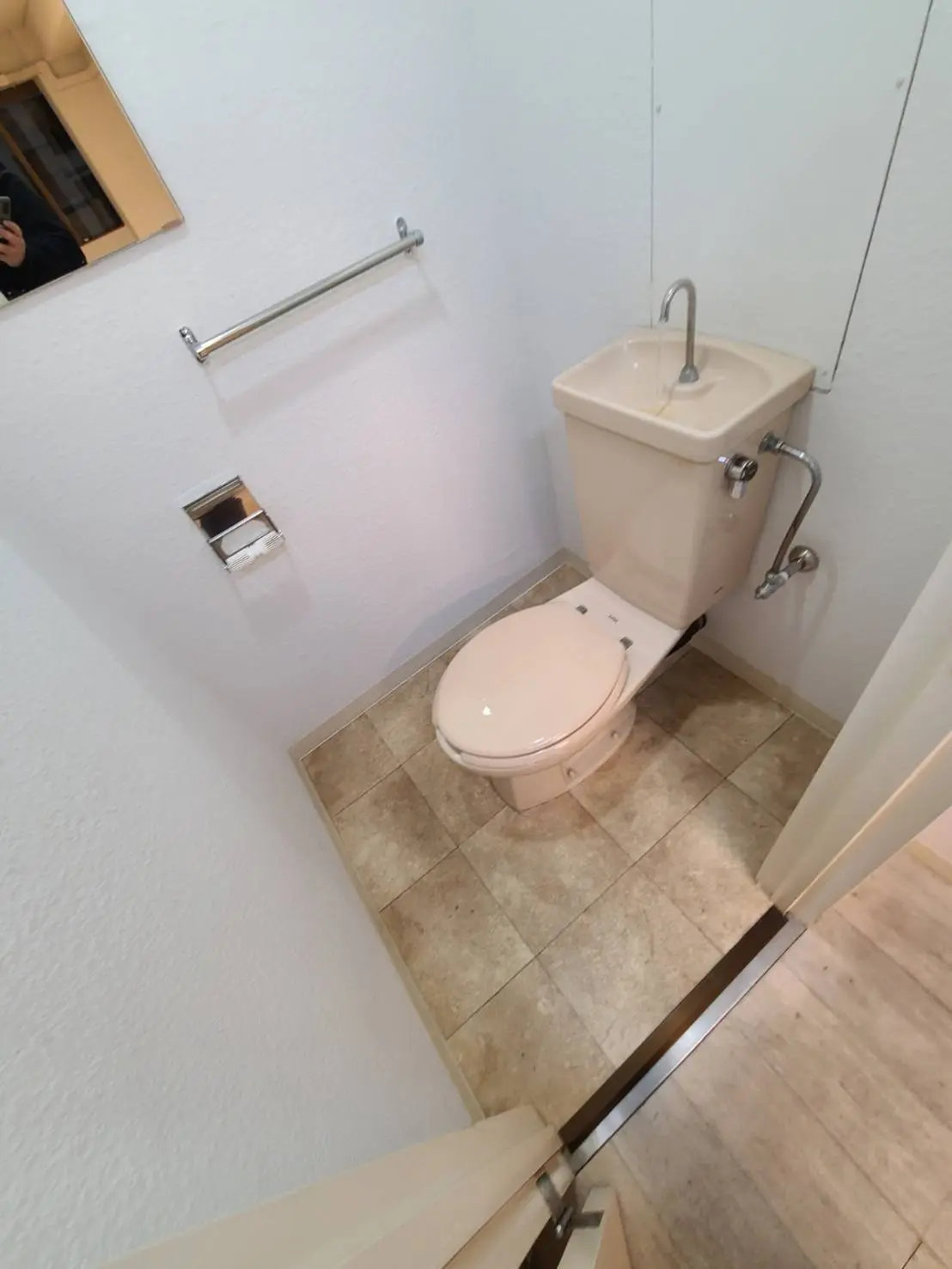 シンプルなデザインのトイレルーム、タンク付き便器とハンドル式水洗、タイル張りの床